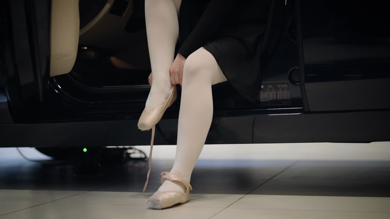 Unrecognizable Caucasian ballet dancer putting on pointes as sitting on driver's seat in car. Elegant woman tying up ballet shoes. Choreography, art, automobile industry.