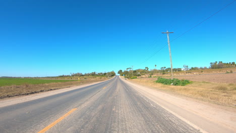 POV-while-driving-past-fields-and-homes-on-a-rural-highway-in-the-Rio-Grand-Valley-of-southern-Texas-on-a-sunny-winter-day