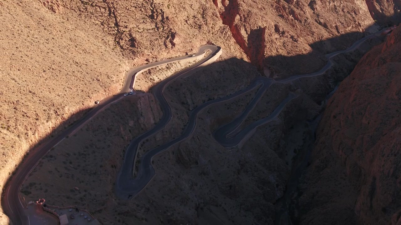High-angle oblique top-down aerial drone shot highlighting the geometric hairpin turns and sharp curves of the famous road in Dades Gorge, Morocco.