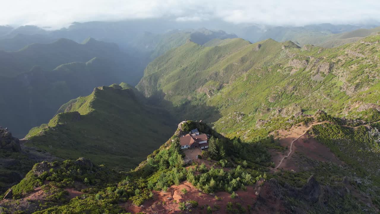 Filmato aereo con panoramica su un rifugio di montagna arroccato sul bordo sotto Pico Ruivo, circondato da vette suggestive a Madeira, in Portogallo. Adatto per viaggi, escursioni e sfondi naturali panoramici