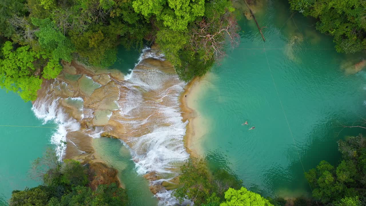 Ripresa aerea dall'alto di persone che nuotano in piscine naturali rocciose con cascate, scena tropicale.