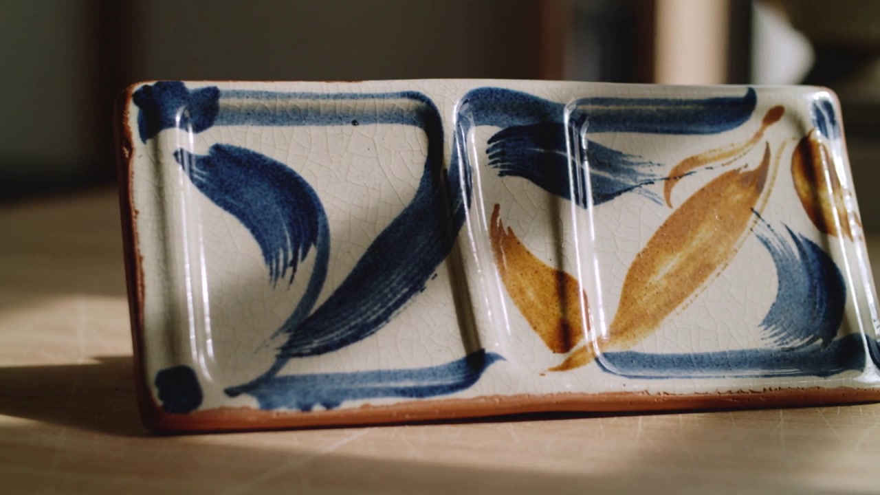 Panning camera revealing divided ceramic dish on wooden table to show glaze crackle and motifs