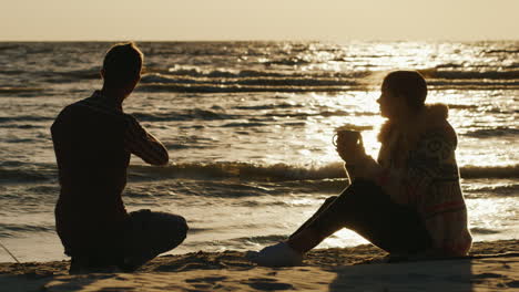 pareja joven romántica relajándose en la playa o en un lago en un día fresco mujer bebiendo té de una taza a