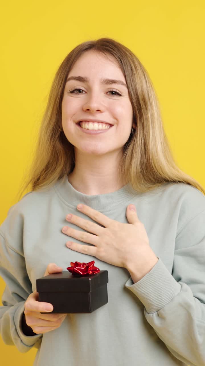 Young woman holding a gift expressing happiness on yellow background