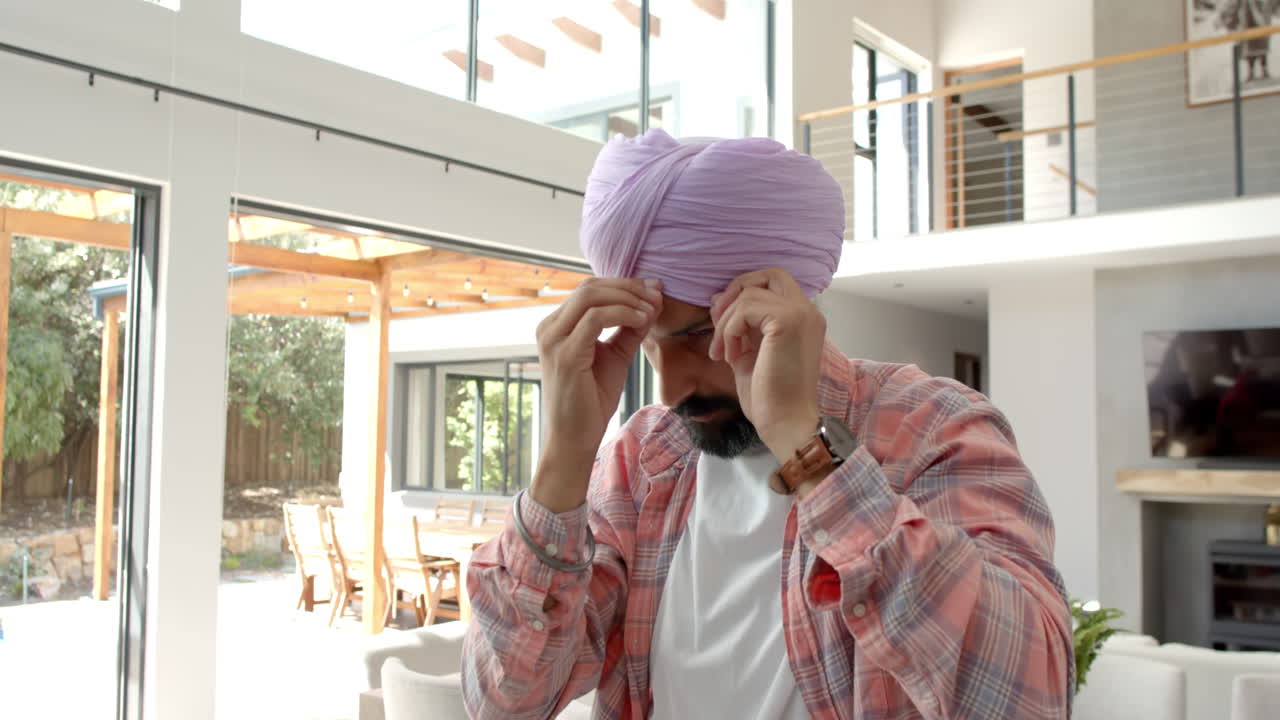 Adjusting turban, man standing in modern home with large windows