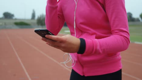 Vista-Lateral-De-Una-Joven-Atleta-Caucásica-Escuchando-Música-En-Un-Teléfono-Móvil-En-Un-Recinto-Deportivo-4k