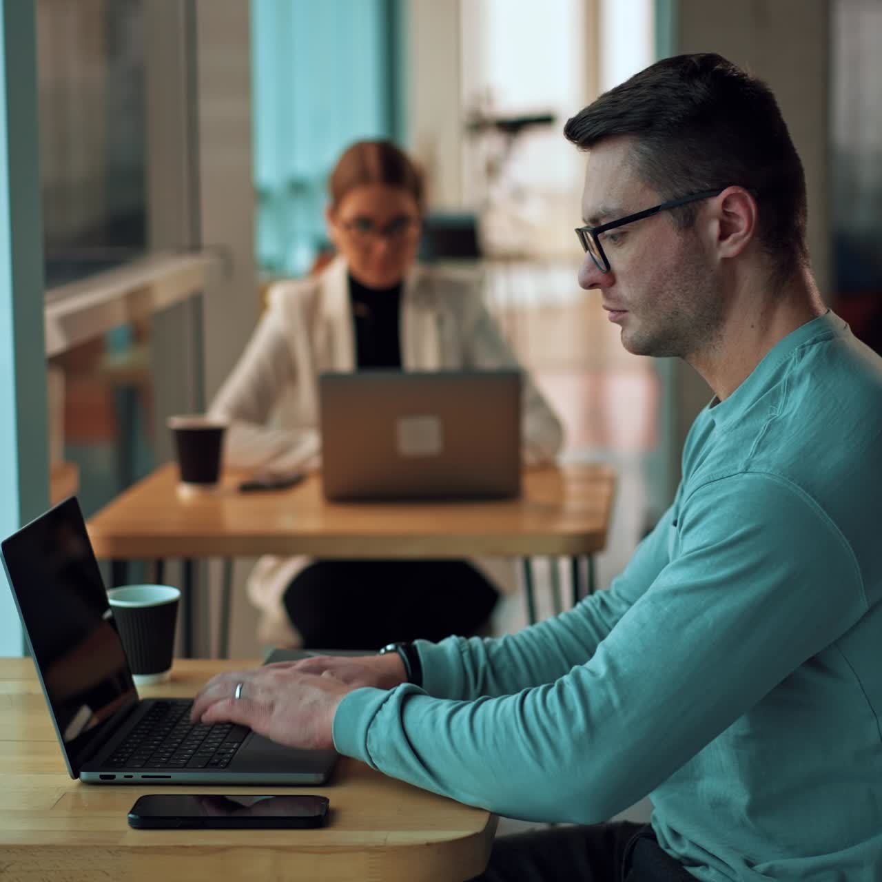 Man sitting at desk leans closer to the notebook in front of him. Male businessman looks at the laptop screen thoughtfully. Female colleague working at backdrop