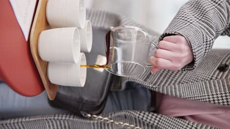 vertical, person in stylish grey coat practices pouring fresh coffee into white cups on tray