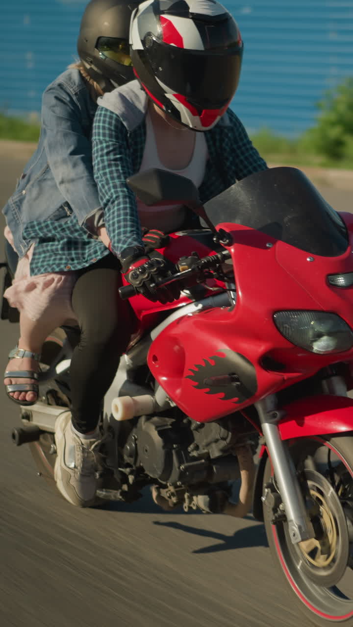 dos damas están montando una bicicleta eléctrica roja, ambas con cascos, mientras viajan a través de un área urbana, sus sombras se proyectan en el suelo mientras mantienen el enfoque mientras avanzan