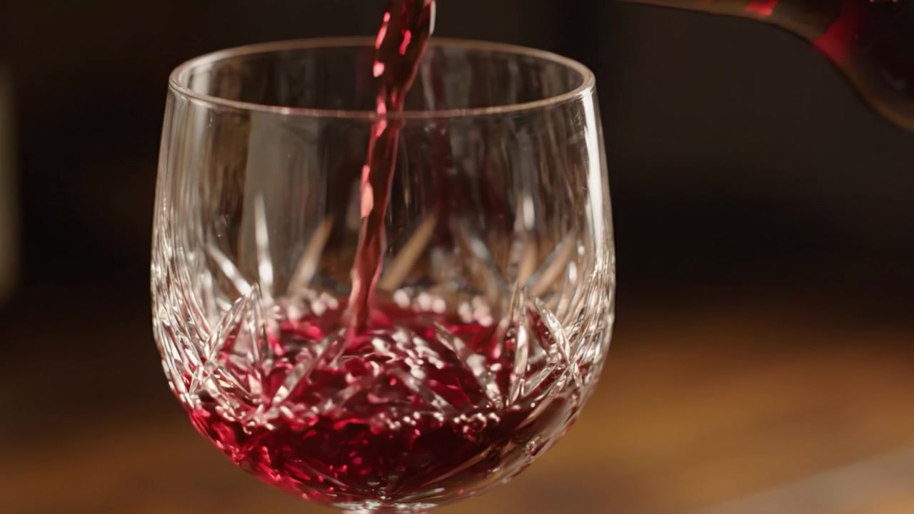 Versamento Squisito: Catturando l'Arte del Vino Versato Elegantemente in un Bicchiere di Cristallo, Mettendo in Mostra Tonalità Ricche e l'Artigianato dei Cristalli