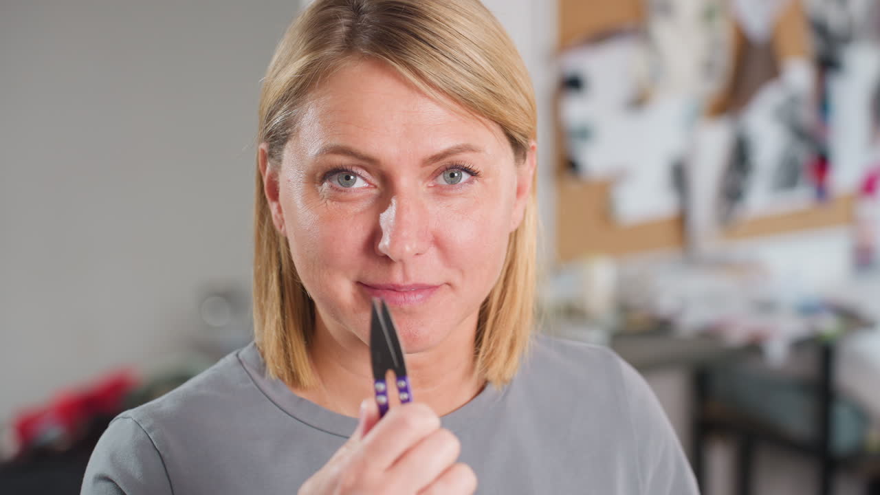 Portrait view of fashion designer smiling confidently while holding clip in hand, gently lifting it up and down, with bright eyes and friendly wink inside vibrant creative workspace