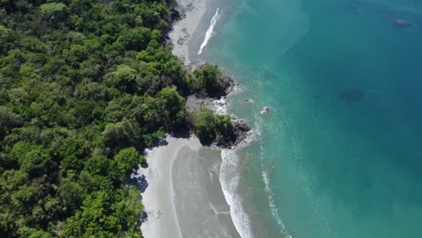 The-coastline-of-Manuel-Antonio-in-Costa-Rica,-with-its-turquoise-waters-crashing-against-the-sandy-beaches-and-the-lush-greenery-of-the-surrounding-forests