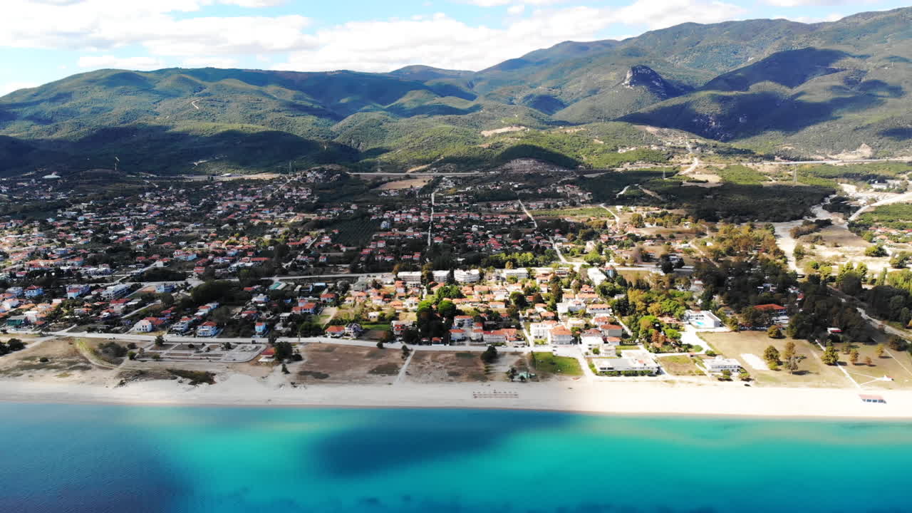 Asprovalta with multiple buildings and greenery, green hills on the background. Aegean sea coast. Long beach along the town. Sunny day. Greece