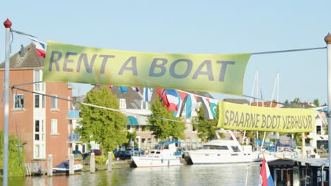 Daytime canal scene in Haarlem, Netherlands with &#039;Rent a Boat&#039; banner, boats, and flags