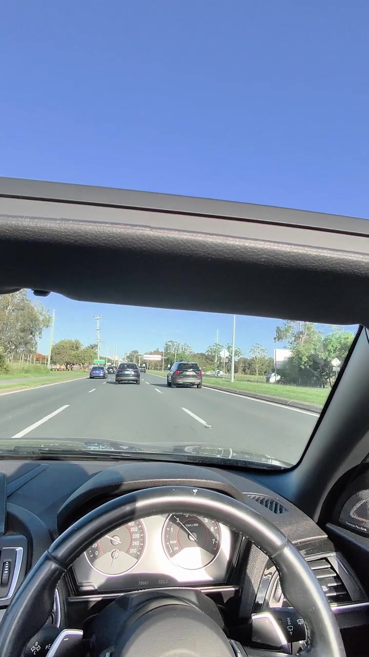 Un conducente percorre una soleggiata autostrada a più corsie in una decappottabile, con vista interna dal cruscotto e un movimento fluido in avanti