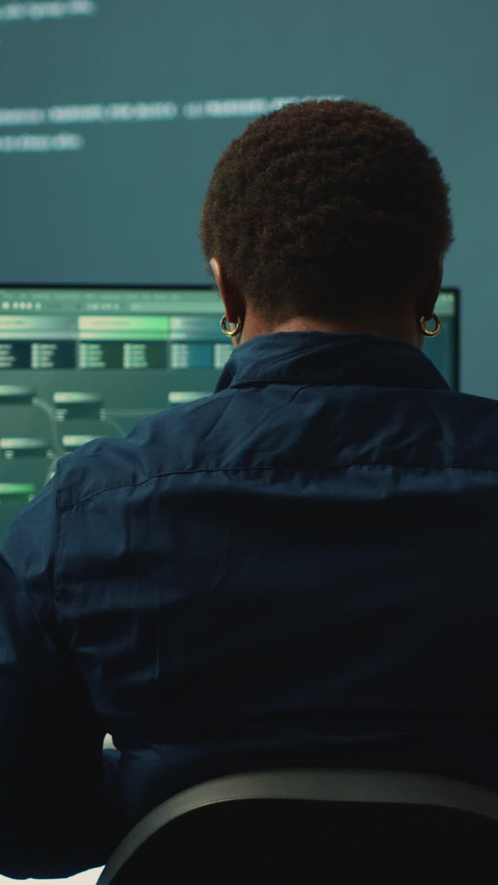 Back View of Programmer Working on Computer Screens in Dark Office