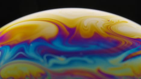 una toma macro de la superficie de una película delgada de jabón con colores de arco iris que crea un hermoso efecto de remolino. semicírculo de una burbuja de sabón con rayas de colores en un fondo negro. primer plano. cámara lenta