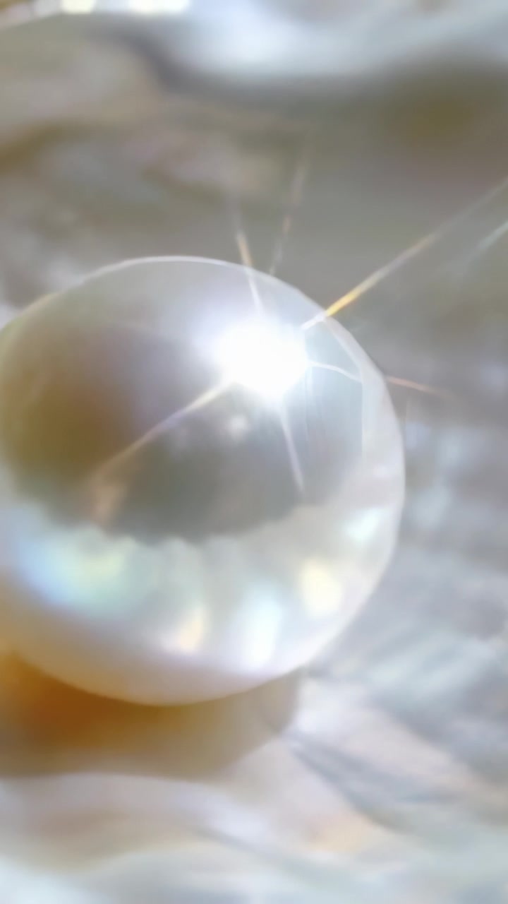 Video verticale: Perla rotonda che sposta un bagliore a stella su un tessuto increspato, con luce fuori campo che causa cambiamenti di tonalità.