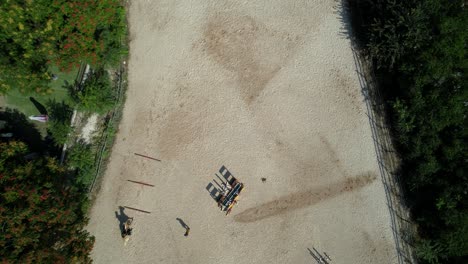 slow aerial descent uncovers a training track where several riders perform jumps under coach observation