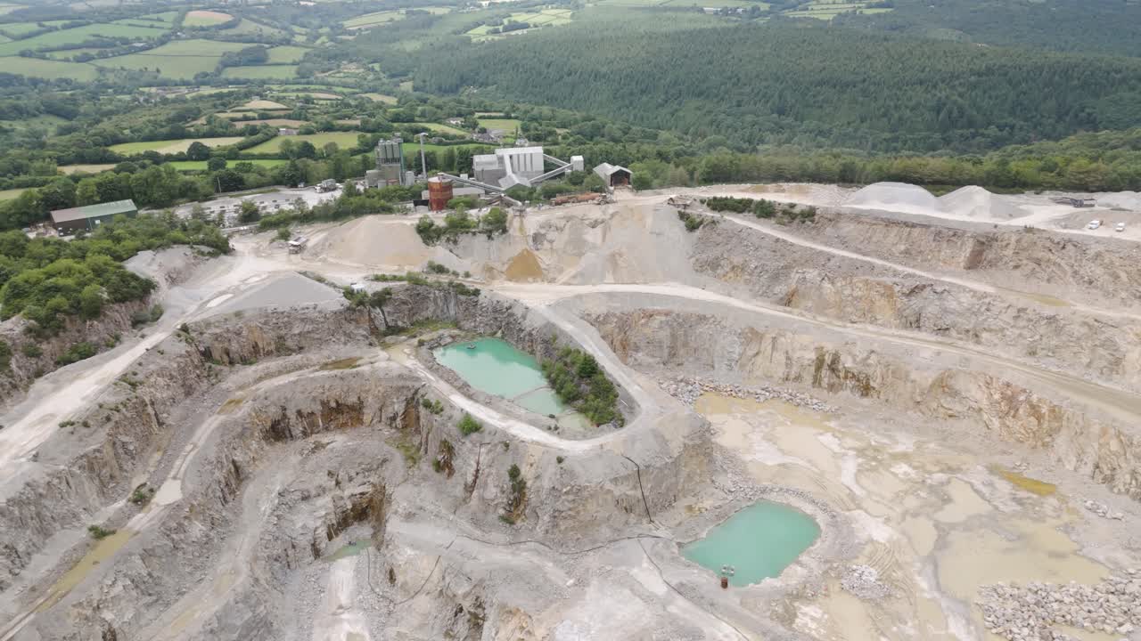 Aerial view of an aggregate mining operation set against a picturesque countryside backdrop with terraced rock layers and industrial machinery