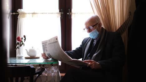 elderly man reading newspaper while wearing a face mask indoors