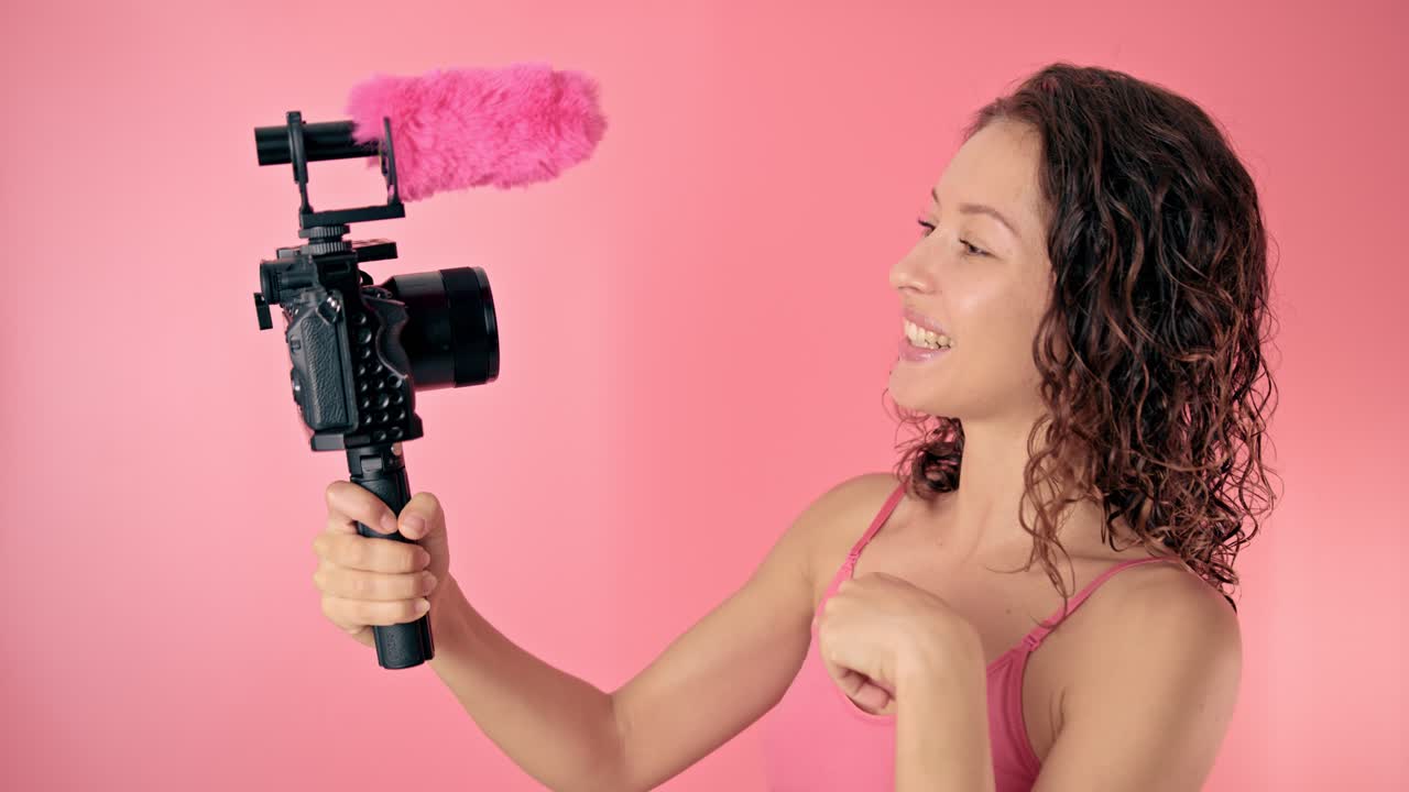 Woman vlogging with pink camera equipment on a pink background