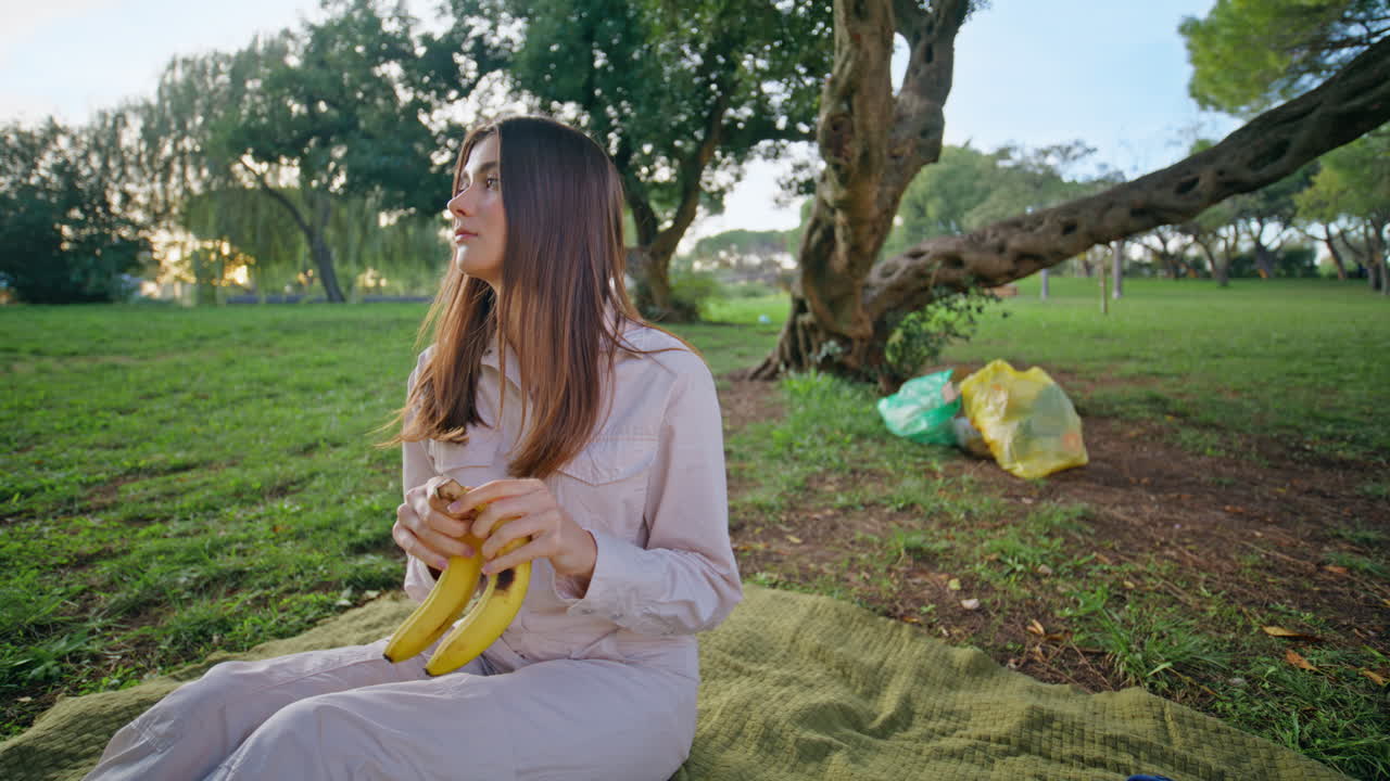 공원 담요 근접에서 휴식을 취하는 바나나를 들고 있는 피크닉 여성. 미소 짓는 젊은 여성