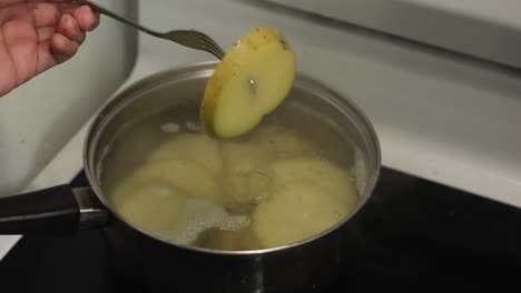 comprobación de patatas amarillas en rodajas con un tenedor, en agua hirviendo