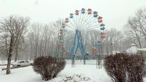 fuertes nevadas en la ciudad, en el parque. vista de la rueda de la fortuna cubierta de nieve en un parque de atracciones vacío en un sombrío día de invierno. grandes copos de nieve están cayendo.