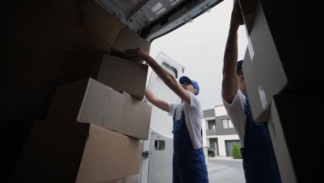 Two young workers of removal company are loading boxes and furniture into a minibus