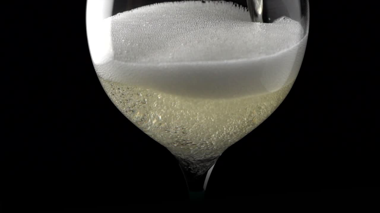 Vino Prosecco sirviéndose en una copa de vino sobre fondo negro con burbujas