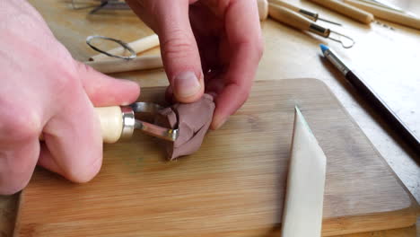 een kunstenaar die met een scherp handgereedschap op bevredigende wijze zachtbruine boetseerklei uitsnijdt terwijl hij in zijn atelier een sculptuur maakt