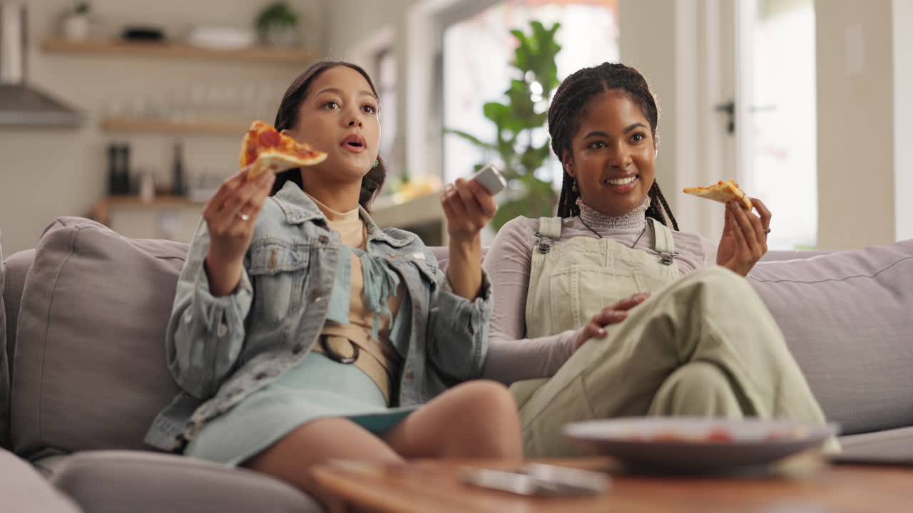Due giovani donne che mangiano pizza e guardano la televisione