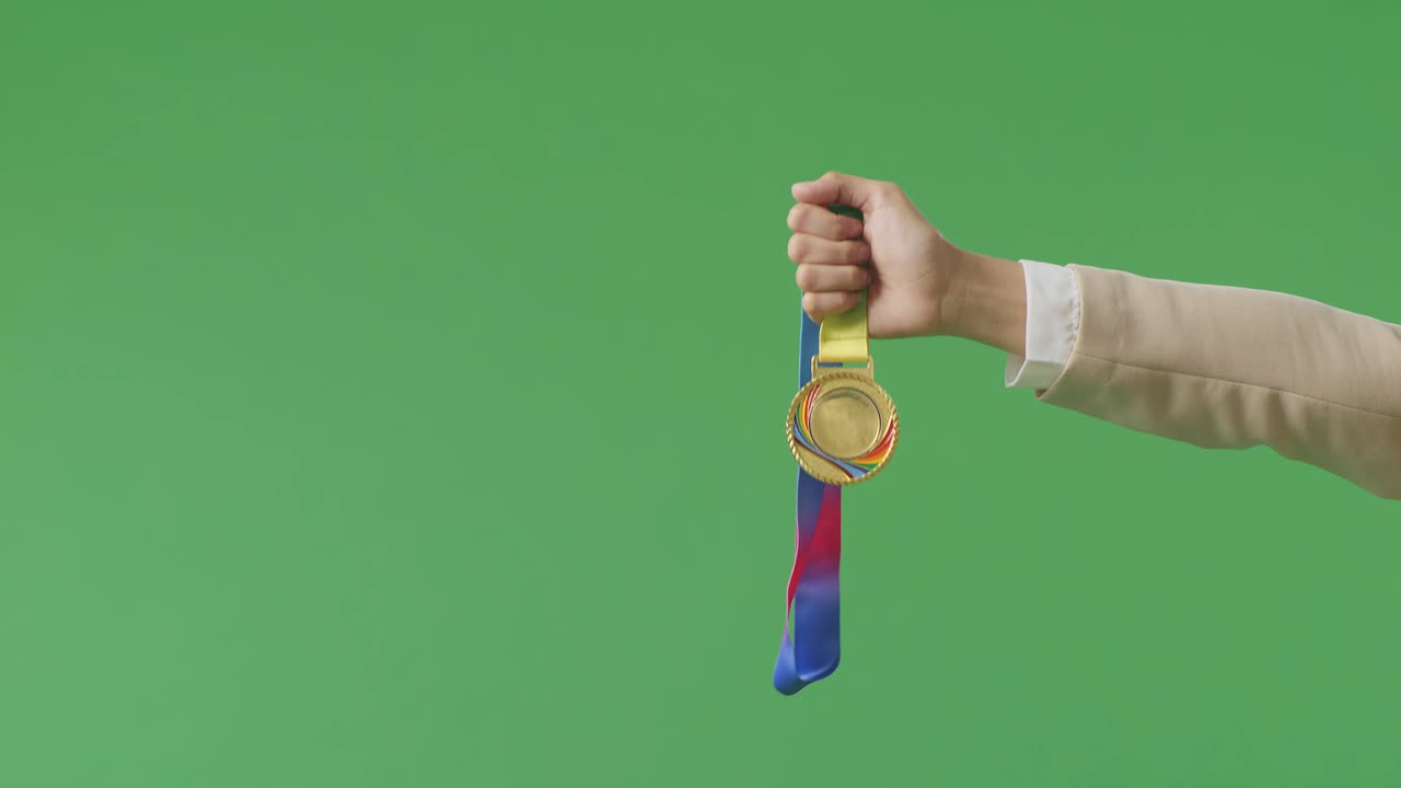 그녀의 에 금메달을 들고 있는 사업가 여성의 손은 스튜디오의 녹색 스크린 배경에서 첫 번째 수상자로 상을 수상하는 것을 보여줍니다.