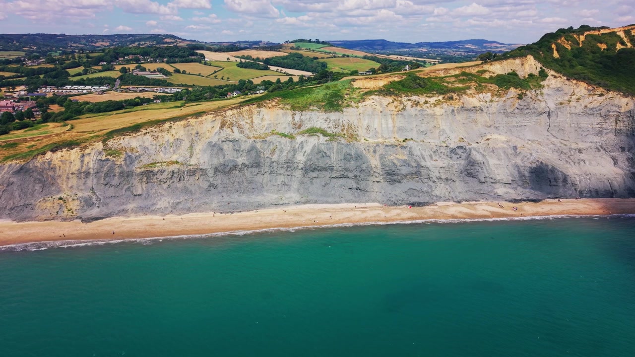 Spettacolari riprese drone di imponenti scogliere costiere, mare turchese e campi ondulati a West Bay sulla Costa Giurassica del Dorset, Inghilterra. Ampio paesaggio aereo che mostra la campagna rurale che incontra.