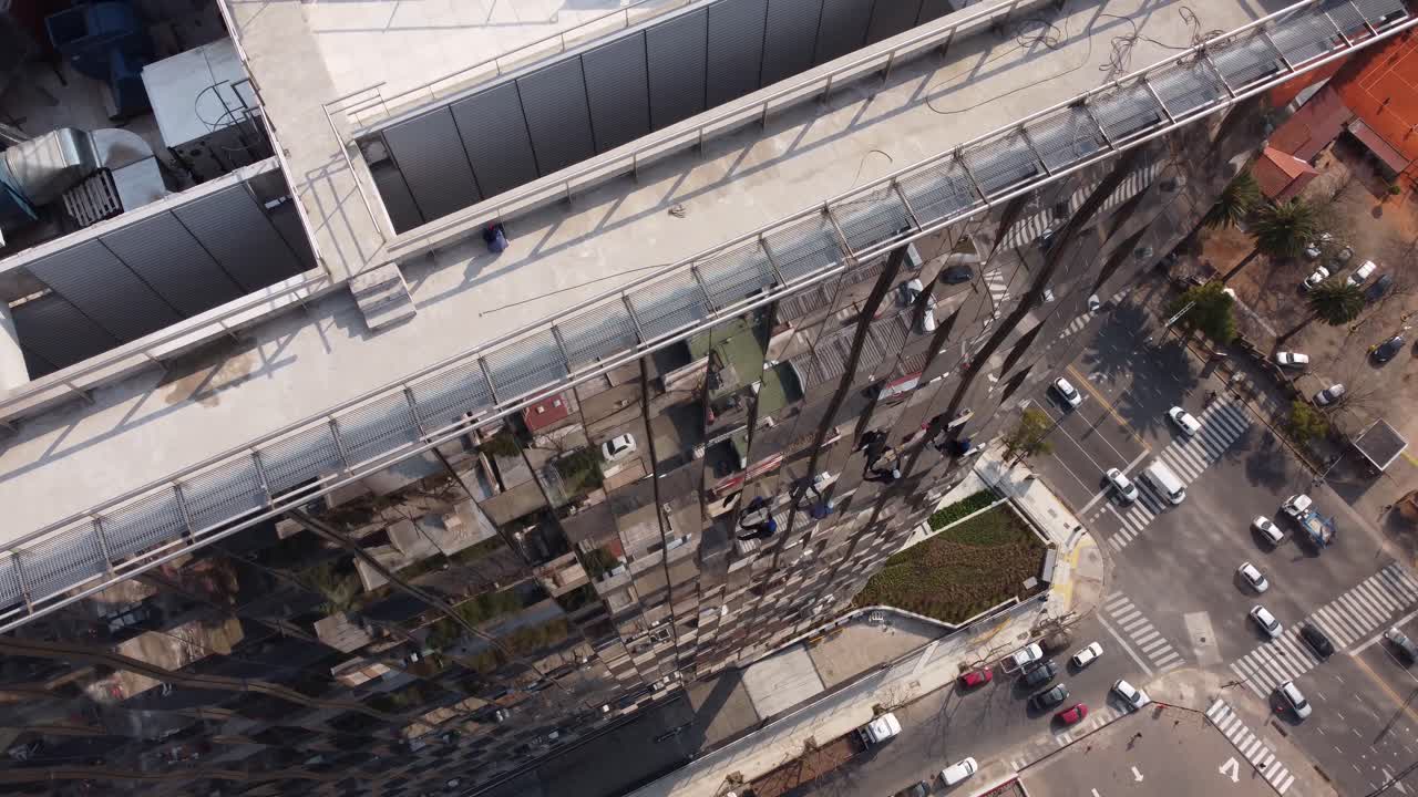 toma aérea de arriba hacia abajo del limpiador de ventanas que lava las ventanas espejadas de los rascacielos durante la conducción de automóviles en la carretera