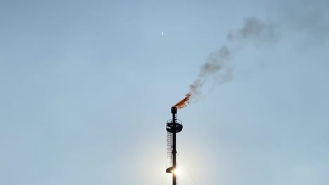 sol brillando detrás de la chimenea de una planta de gas, quemando gases y causando contaminación del aire, una imagen impactante sobre el cambio climático y sus efectos