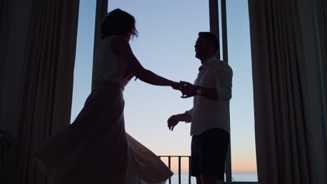 silhouette happy couple dancing in hotel room at sunset enjoying honeymoon vacation having fun celebrating on holiday with beautiful ocean view