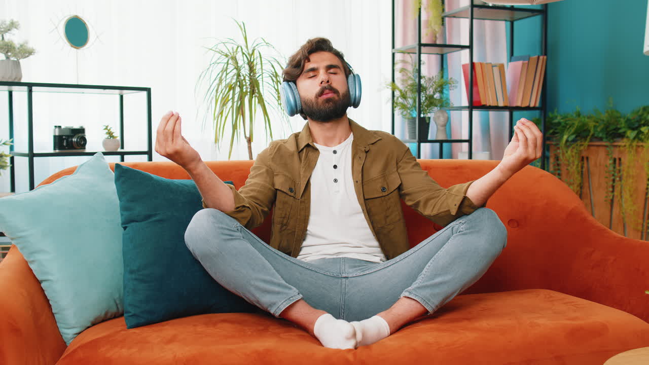 Arabian man listening music, breathes deeply meditating with concentrated thoughts peaceful at home
