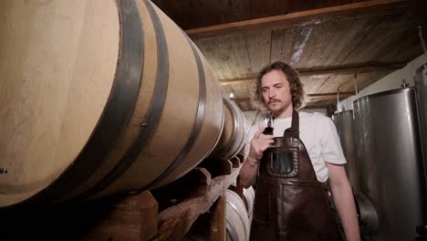 authentic shot of successful male sommelier is tasting a flavor and checking white wine quality poured in transparent glass in a wine cellar.