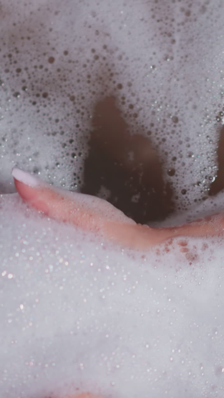 Woman takes fluffy foam in bathtub closeup. Playful lady enjoys cozy bath with soap froth in bathroom. Woman rests caring of body and skin at home