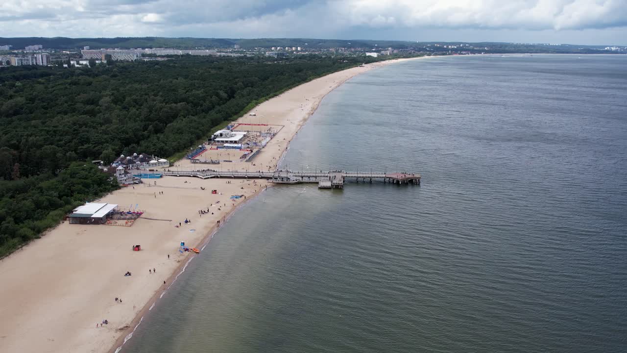 Drone avanza lungo una spiaggia sabbiosa, un molo di legno, il margine di una foresta e il Mar Baltico