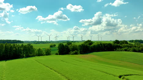 aerial shot of expansive green fields with wind turbines under a partly cloudy blue sky