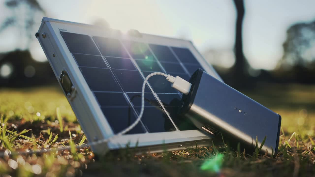 Harvesting sunlight foldable solar panel charging power bank on park grass with white USB cable