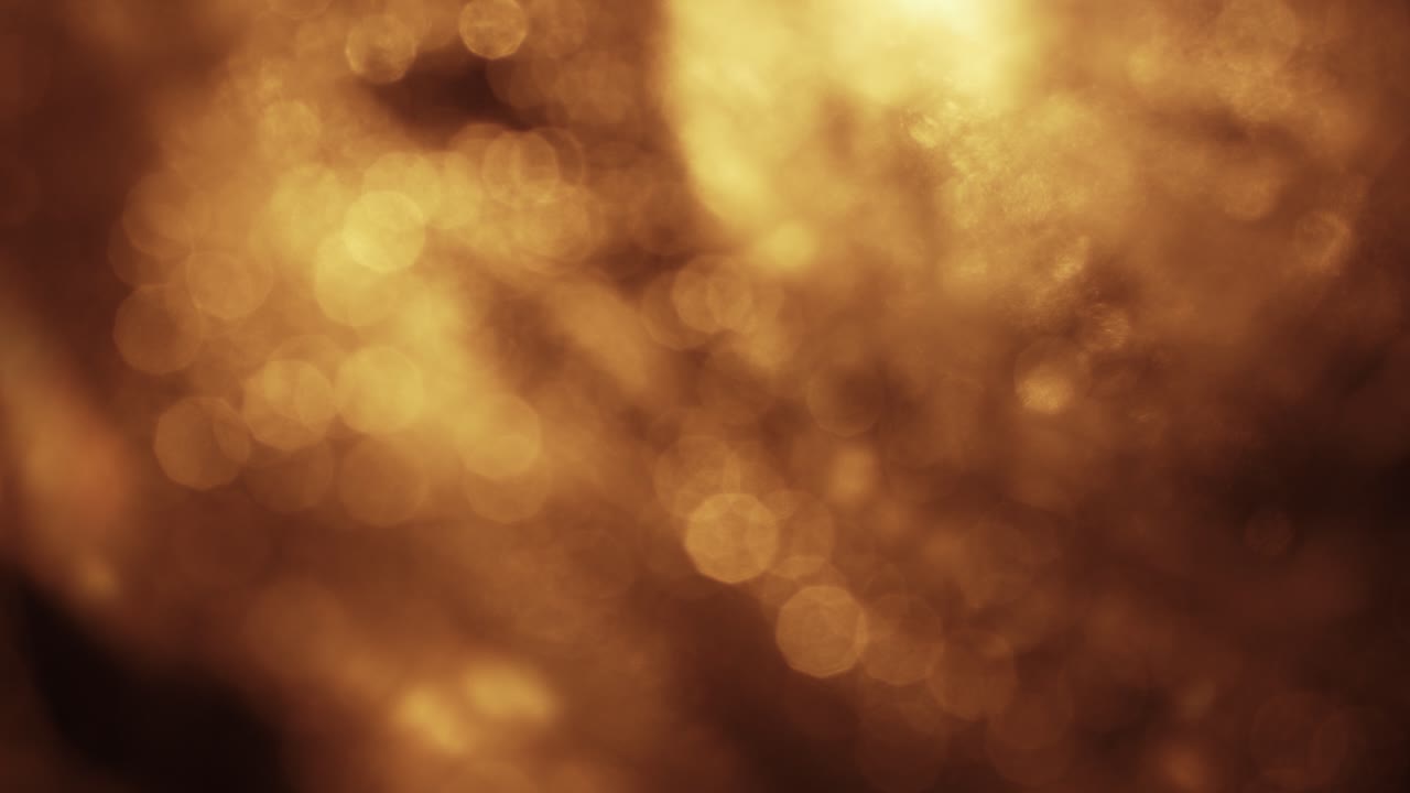 Glimtende gyldne bokeh-lys partikler på sort baggrund.