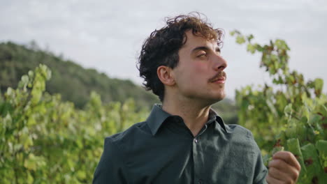 Winegrower-eating-ripe-grapes-at-plantation-close-up.-Young-man-tasting-harvest.