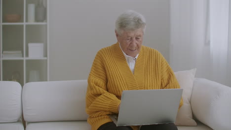 senior woman with gray hair make video call using laptop at home. elderly woman having a video call with family smiling and waving. covid 19 stay connected. online chatting with friends