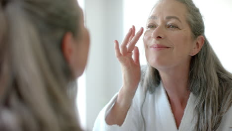 a mature caucasian woman with gray hair applying makeup