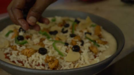 hand sprinkling fresh olives pieces on fresh pizza