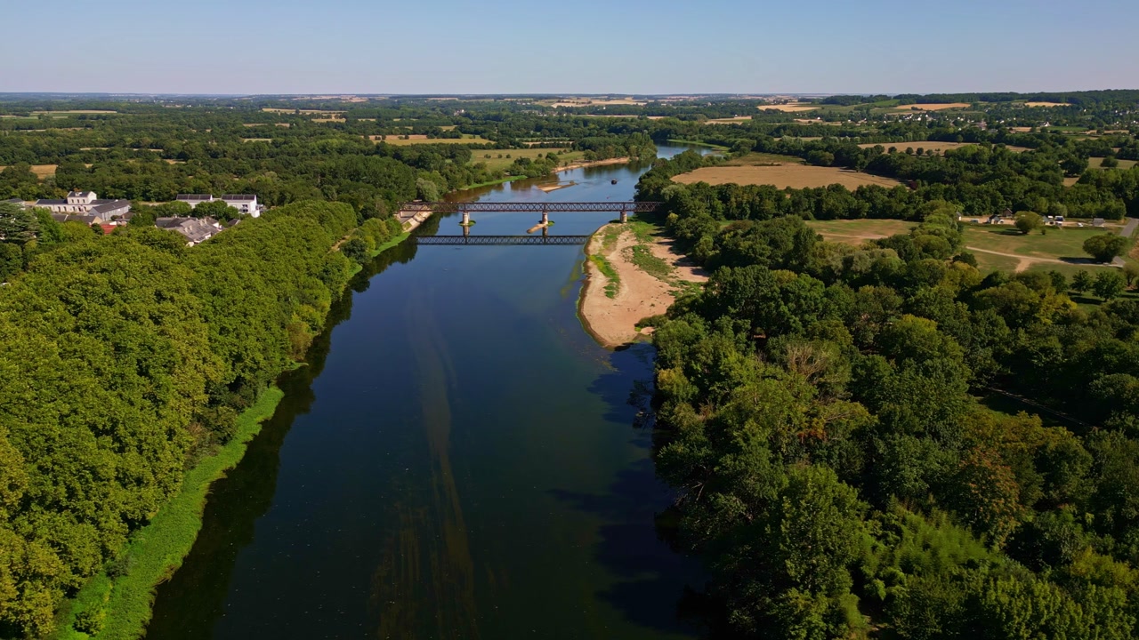 Lateral drone shot showing the Vienne River, bridge, riverbanks, trees, and surrounding forest near Chinon.